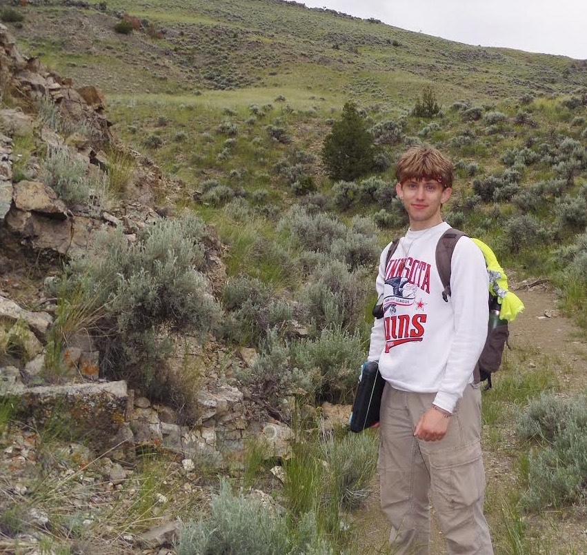 A young man standing near an outcrop 